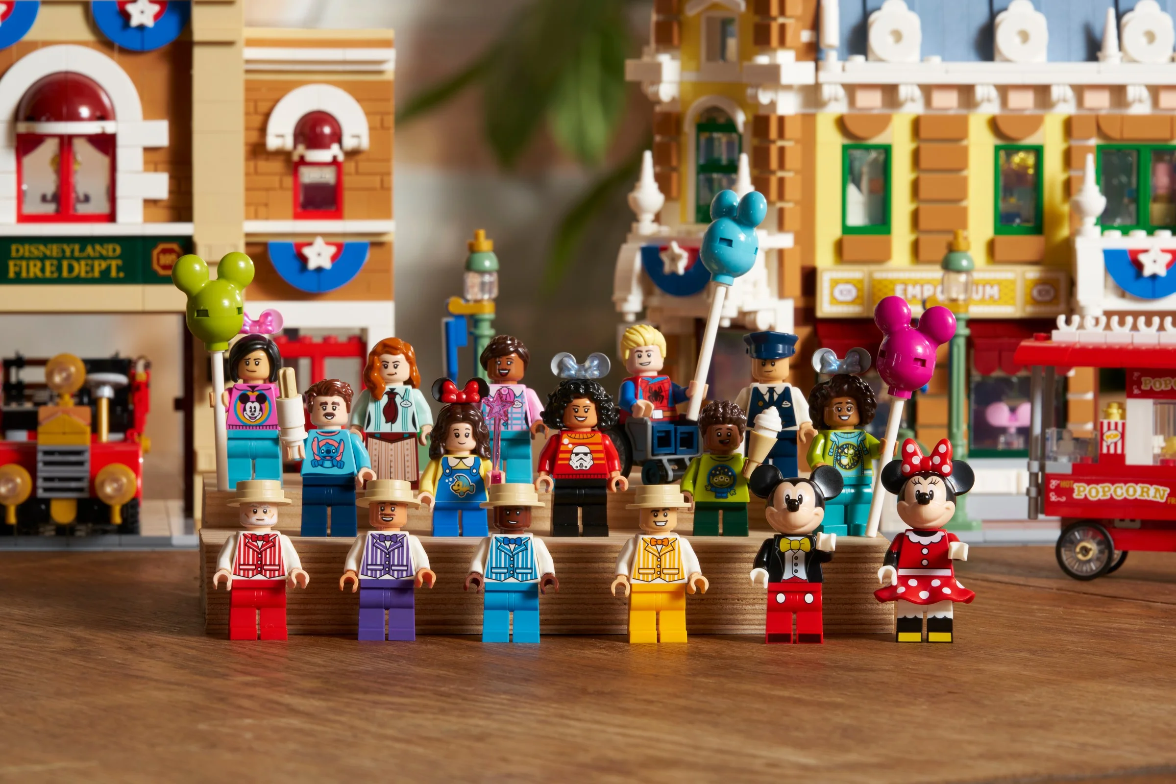 Prezentare a numeroase minifigurine LEGO Disney Main Street, U.S.A., cu clădirile pe fundal.