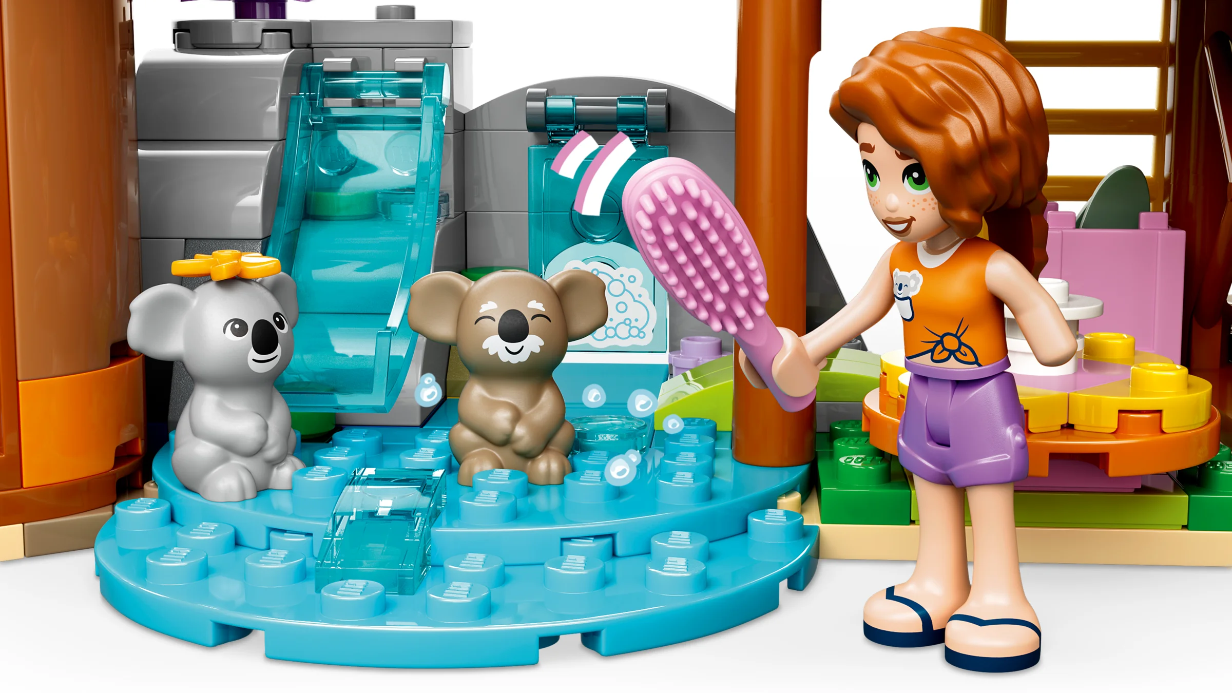 O minifigurină LEGO Friends perie un koala lângă o zonă de îngrijire, cu tobogan și duș.