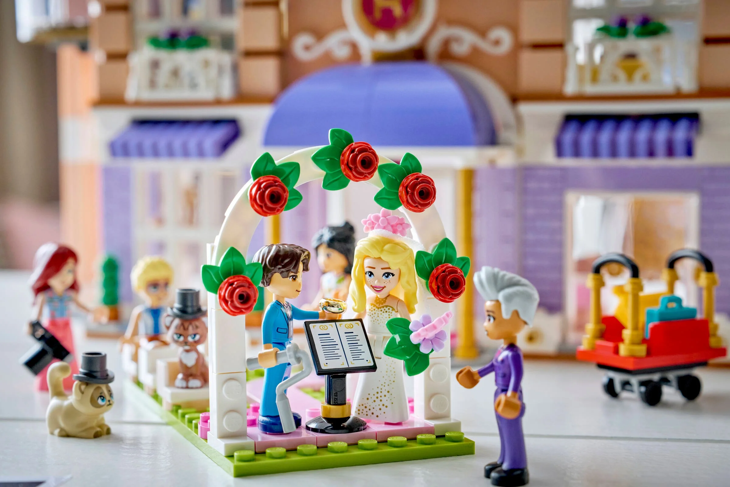 Scenă nunta la hotel. Minifigurine mire și mireasă sub arcă cu flori. Atmosferă festivă, plină de detalii.