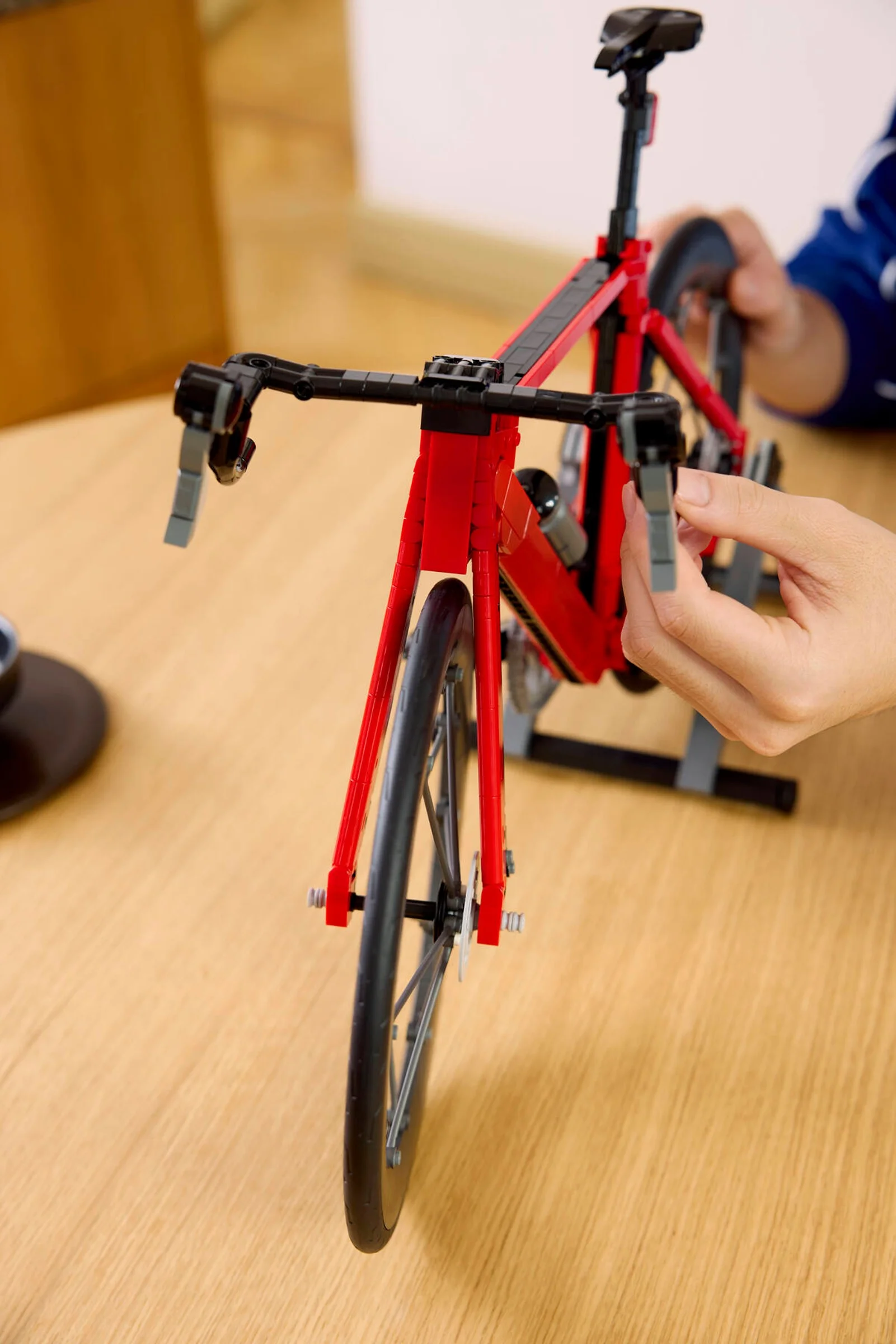 Prim plan al bicicletei de curse LEGO, roșie și neagră, cu detalii fine și mâini care o ajustează.