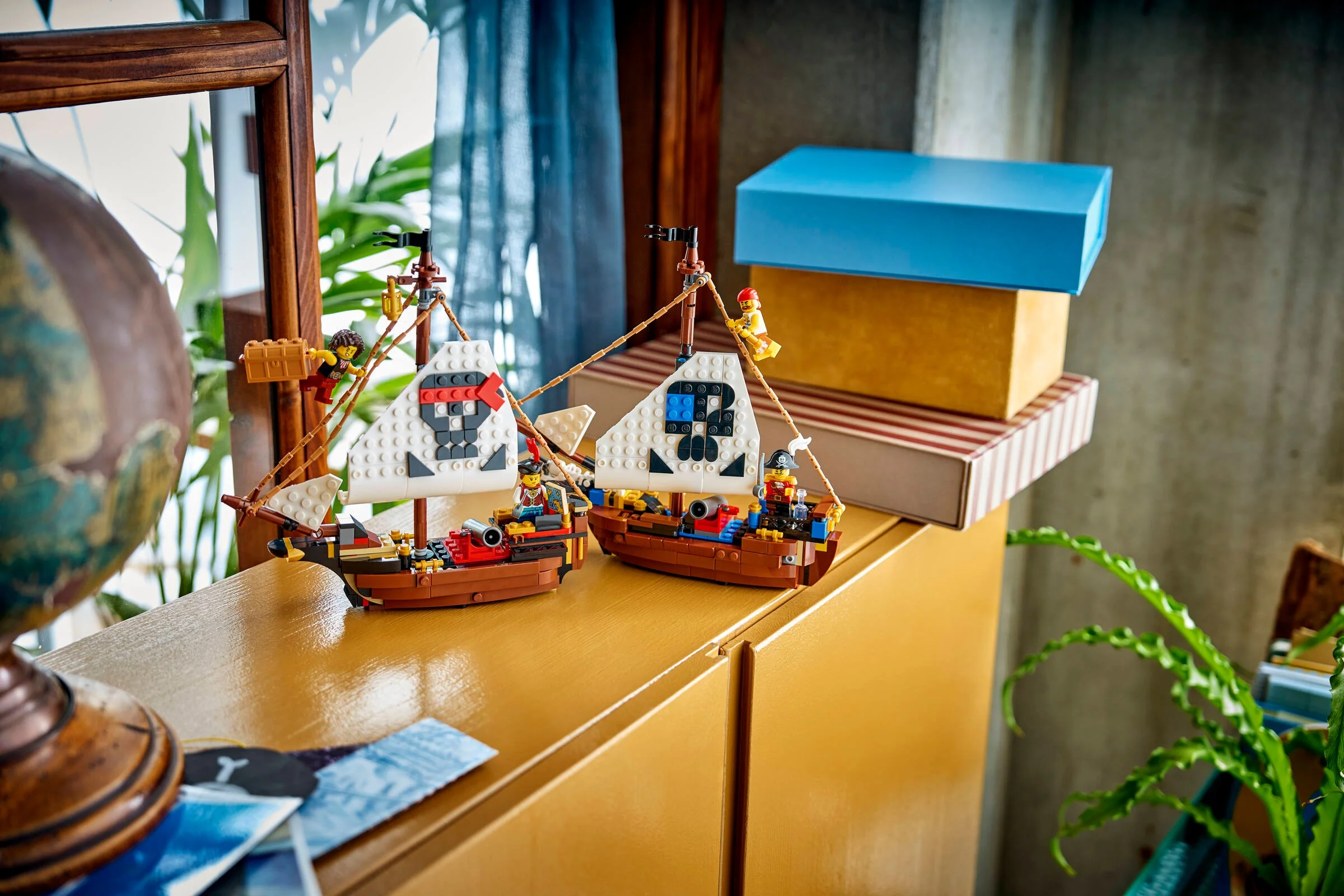 Două corăbii pirate LEGO expuse pe o mobilă, cu minifigurine și detalii vizibile.