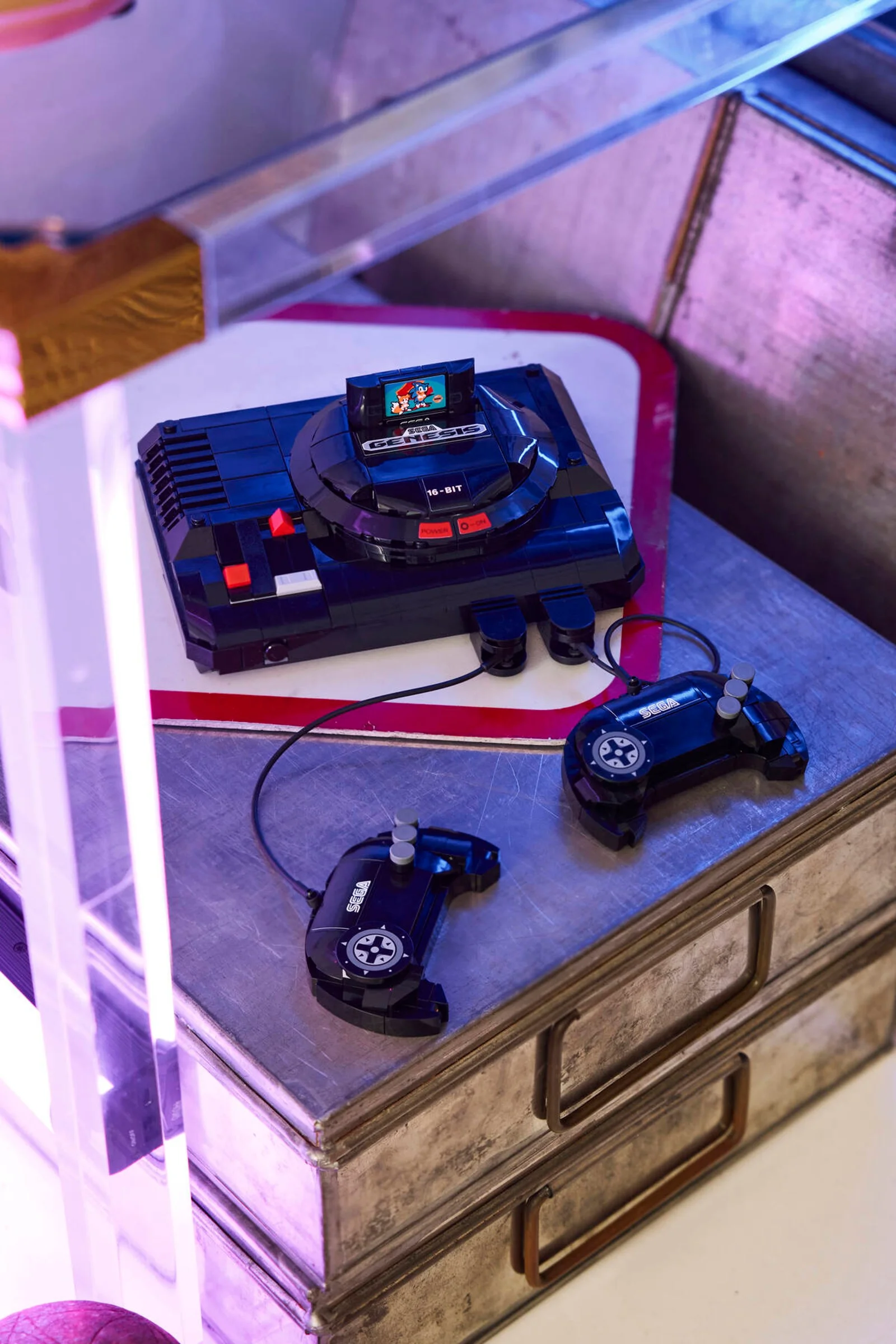 Imagine cu consola SEGA Mega Drive LEGO și două controllere pe o masă metalică, detaliată.