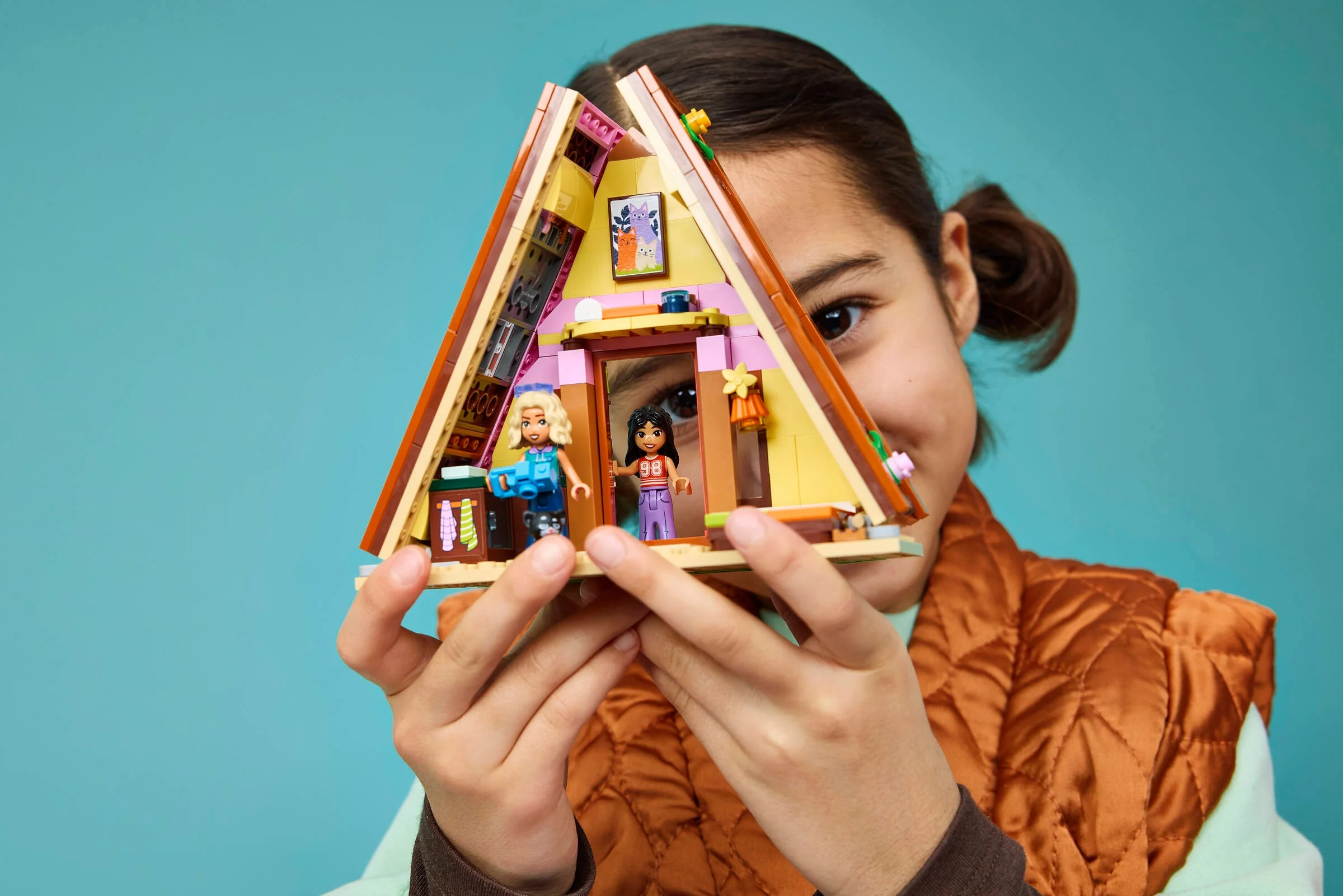 O fată ține cabana glamping LEGO, evidențiind interiorul detaliat. Cabină drăguță!