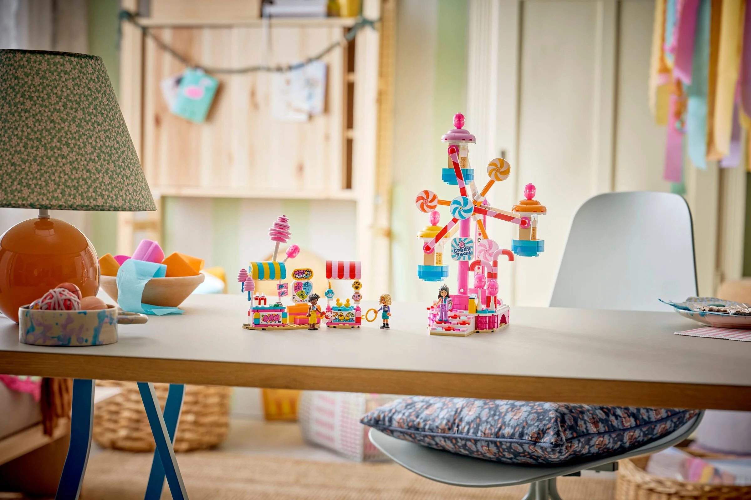 Imagine cu LEGO Friends 42700: un carusel și standuri de dulciuri colorate, pe o masă, într-o cameră.
