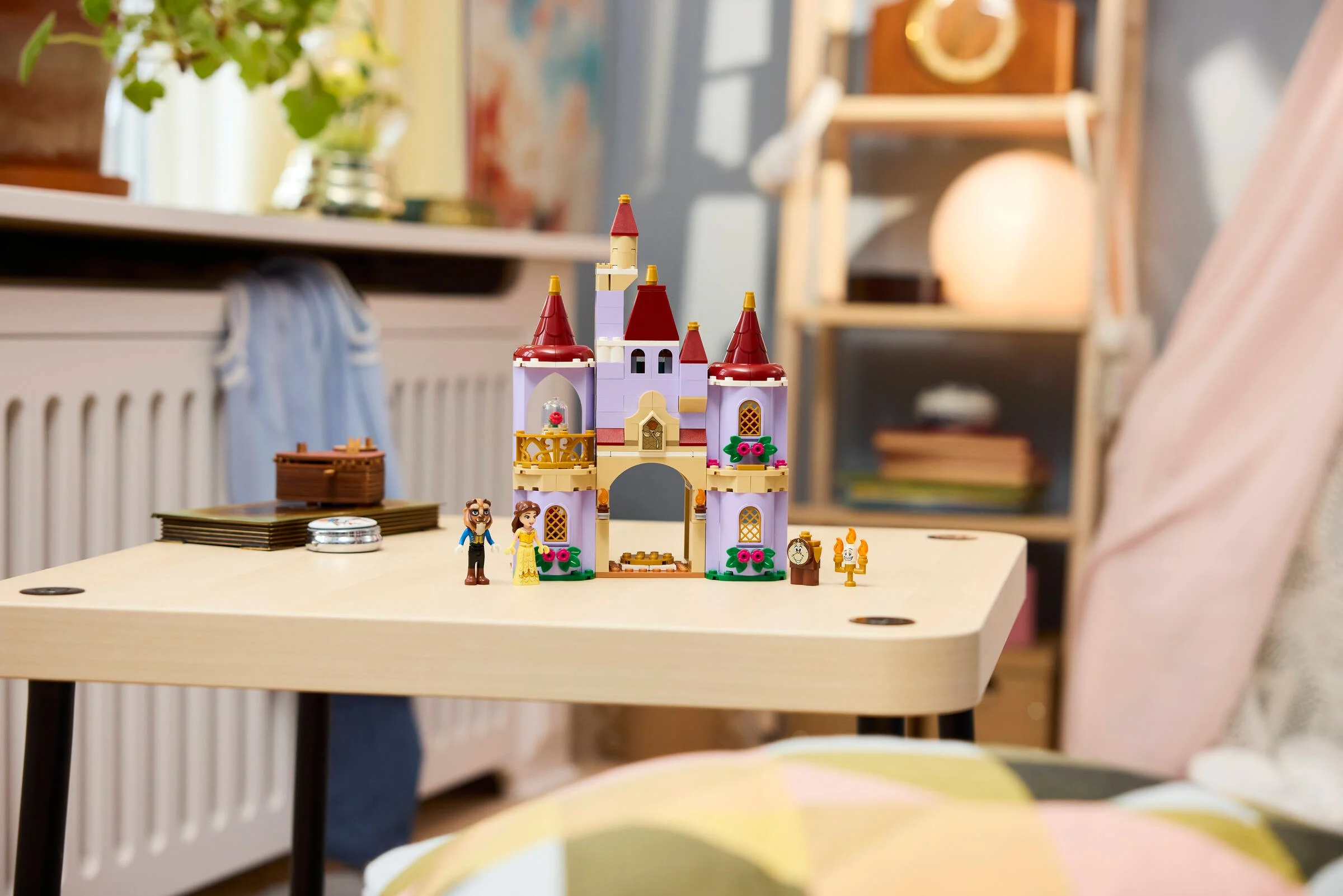 Castelul fermecat al lui Belle și a Bestiei LEGO, aranjat pe o masă de copii, cu mini-figurinele.