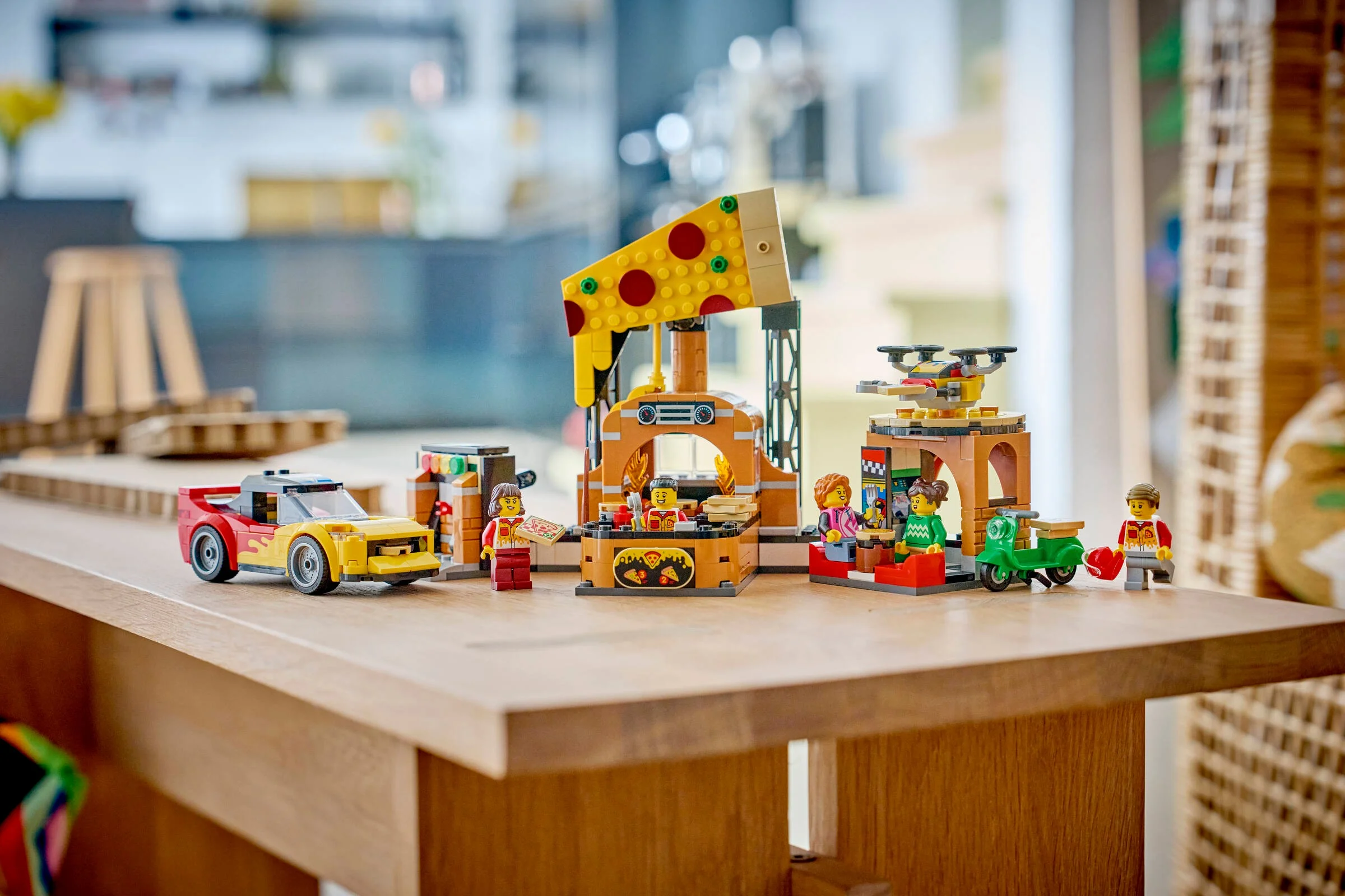 Setul LEGO 60496 Experiența Livrării de Pizza include pizzeria, mașină, scuter și minifigurine.
