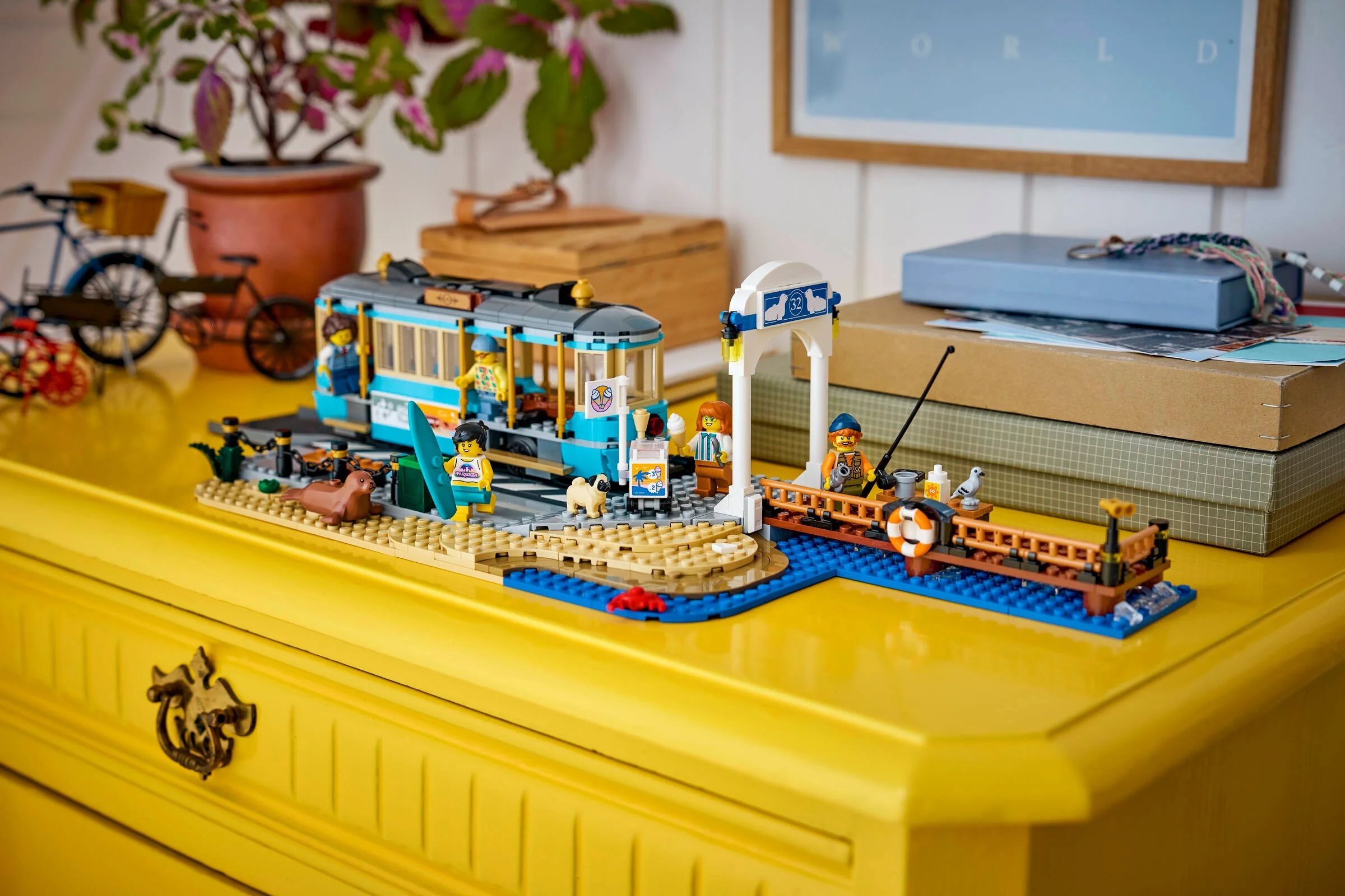 Setul LEGO 60506: Tramvaiul Plajei, cu minifigurine și detalii, aranjat pe o comodă galbenă.