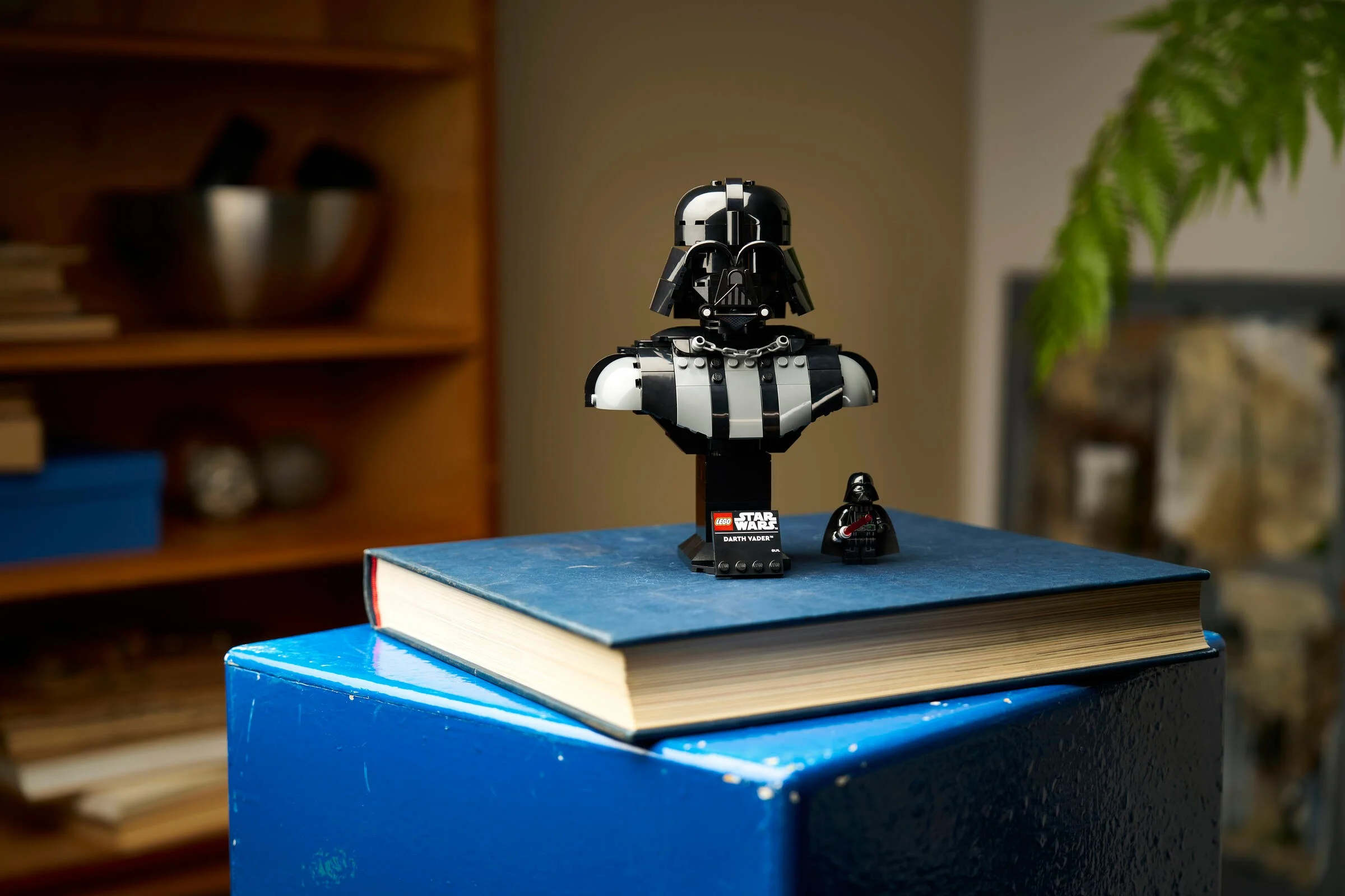 Bustul LEGO Darth Vader și minifigurina, așezate pe o carte albastră. Model detaliat.