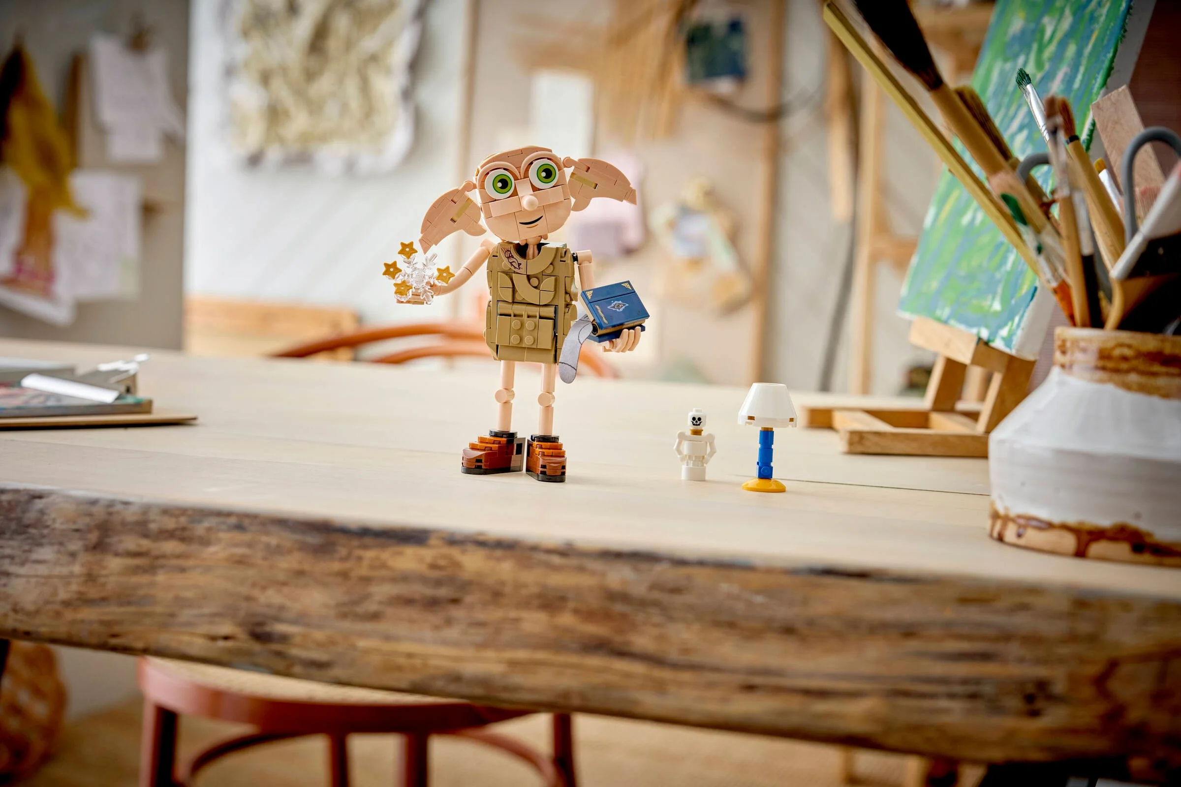 Dobby, elful liber, stă pe o masă alături de un schelet și o lampă. Set LEGO Harry Potter.