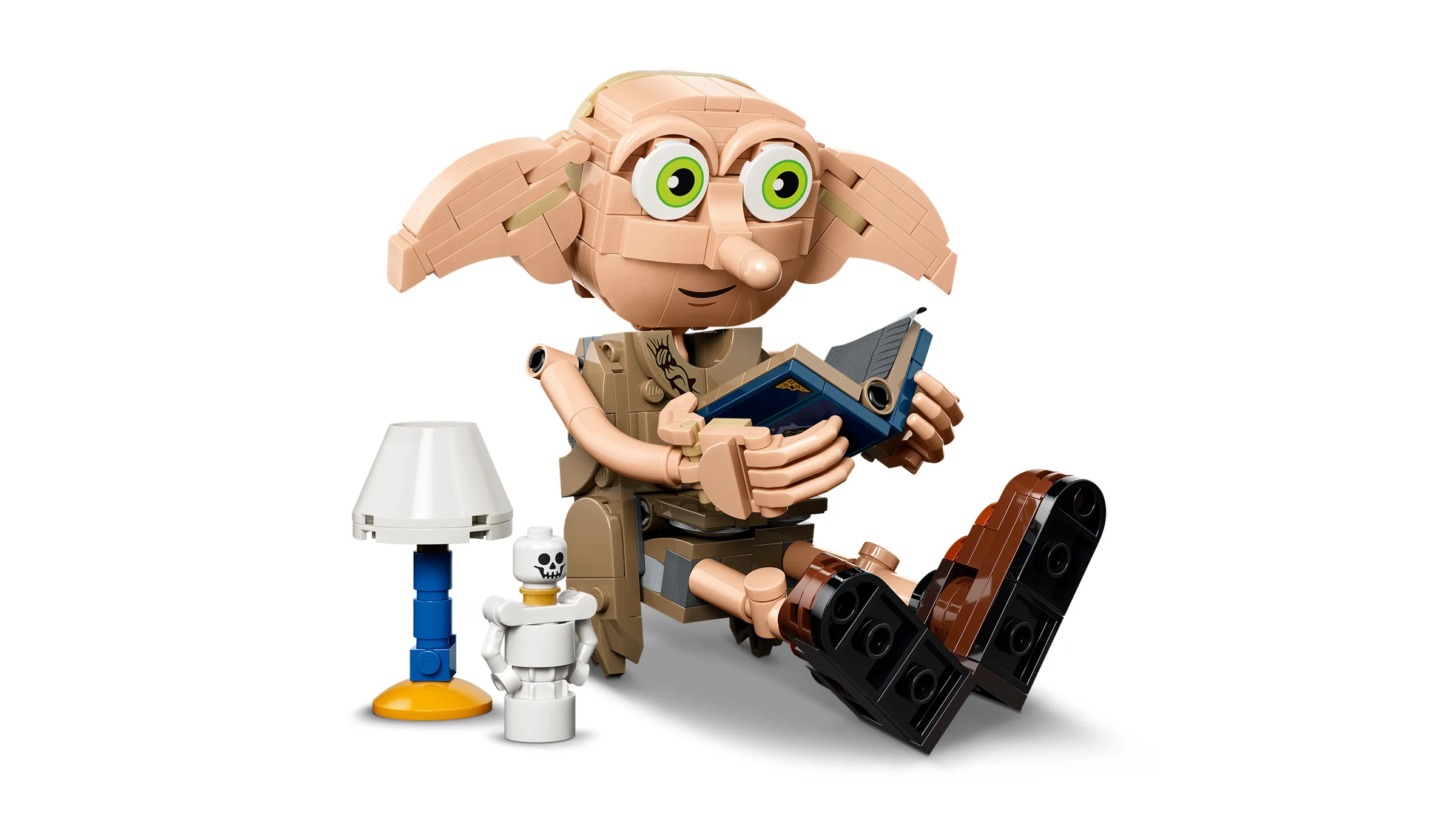 Dobby, spiridușul liber, stă așezat și citește o carte, lângă o lampă și un schelet mic.