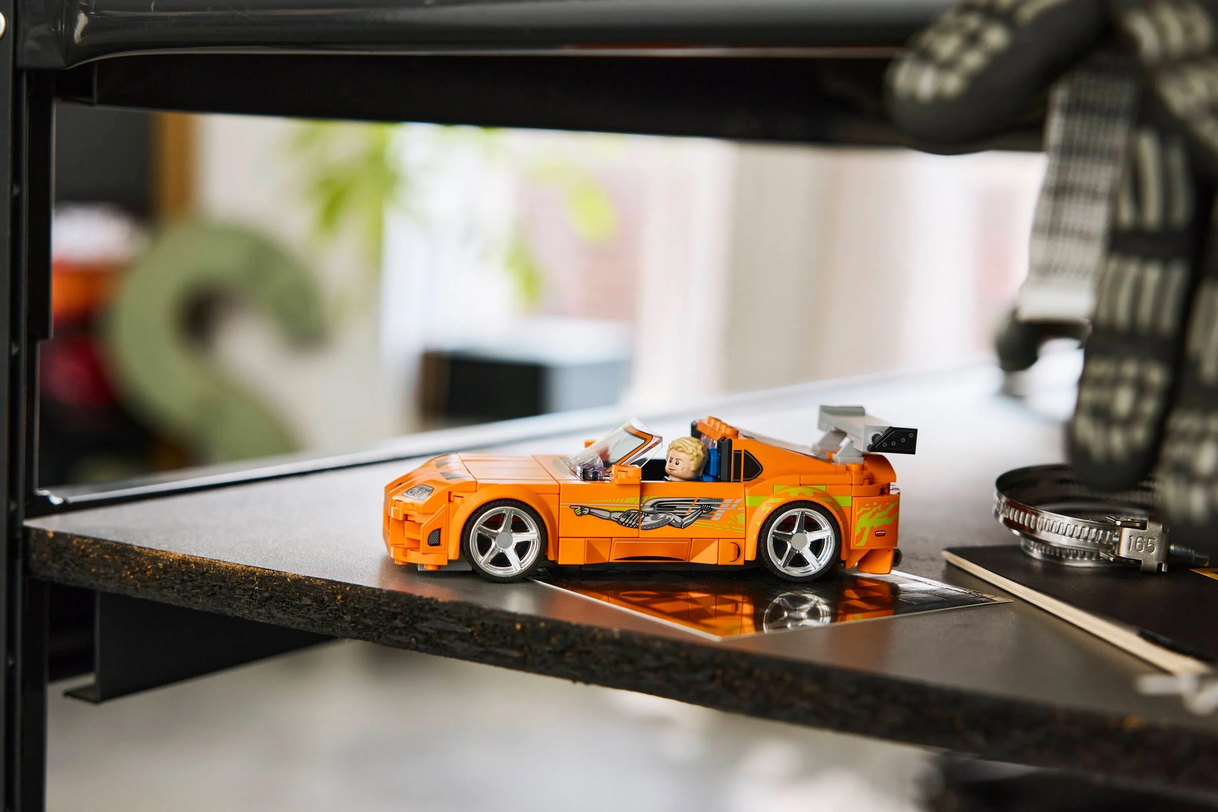 O imagine cu Toyota Supra MK4 portocalie, complet asamblată, pe o poliță. Minifigurina e la volan.