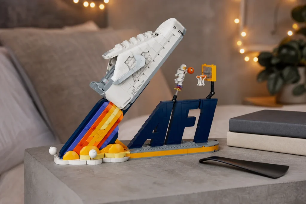 Macheta din piese LEGO a pantofului Nike Air Force 1 expusă pe o noptieră modernă din beton gri, luminată cald de o ghirlandă de beculețe difuze în fundal.