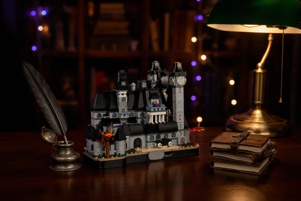 Setul LEGO 76788 Academia Nevermore este expus pe un birou gotic din lemn masiv, luminat de o lampă de birou și decorat cu o călimară cu pană și jurnale vechi.