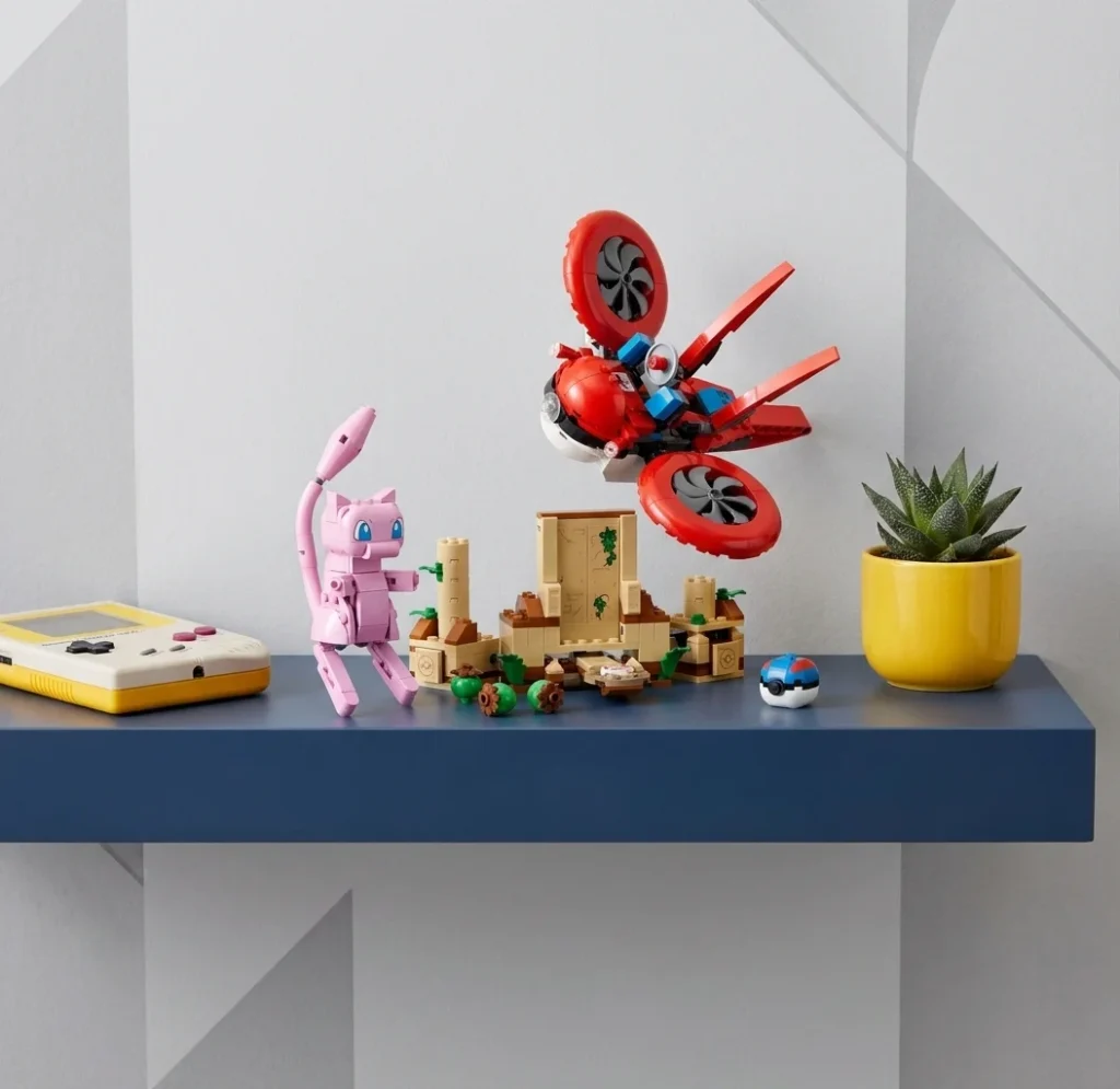Setul LEGO Pokémon 72161 Căutarea cu drona a miticului Mew așezat pe un raft albastru din dormitorul copiilor, alături de o consolă de jocuri retro și o mică plantă suculentă în lumină neutră.